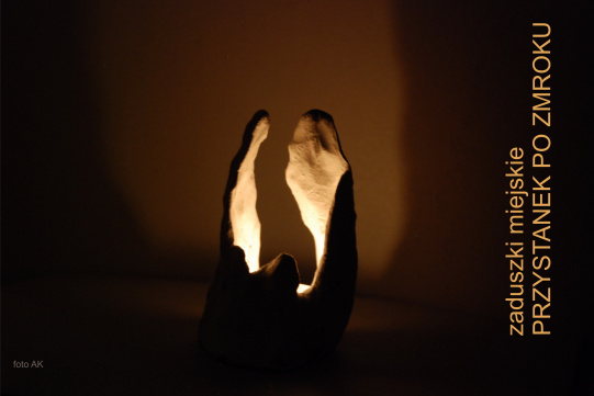 artystyczna świeca zapalona w ciemnym pomieszczeniu i napis "zaduszki miejskie, przystanek po zmroku"