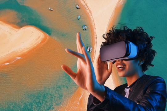 na 1. planie osoba w googlach do oglądania wirtualnej rzeczywistości wyciąga rękę, w tle abstrkcyjnie wyglądająca plaża z lotu ptaka