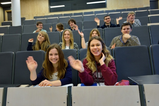 studenci siedzący w audytorium machający do aparatu