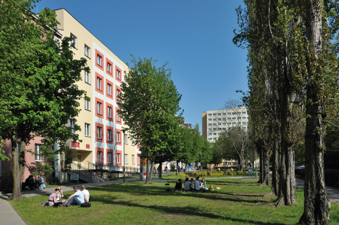 The photo shows the dormitory building. In the foreground, you can see students sitting on the green grass.