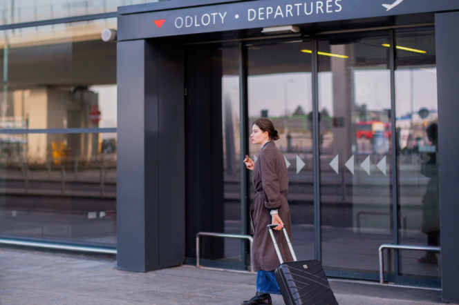 Na zdjęciu widać młodą kobietę z walizką przy wejściu na lotnisko