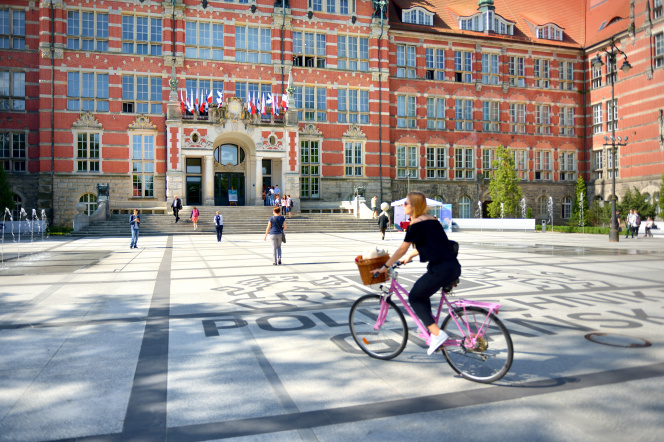 Kobieta na różowym rowerze przed Gmachem Głównym 