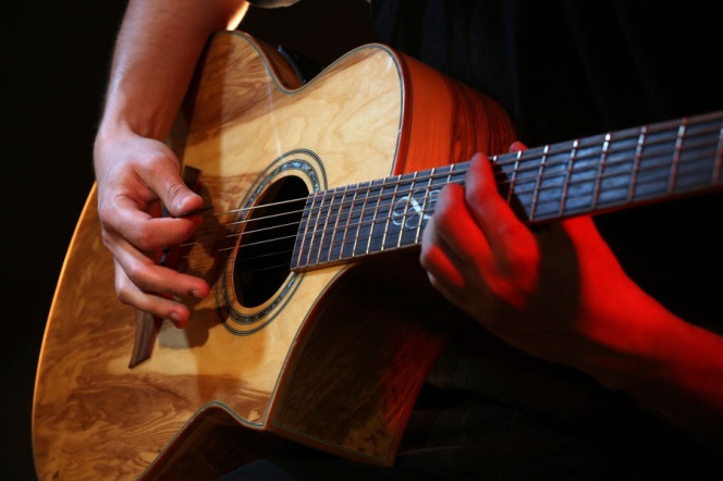 Gitara akustyczna trzymana przez dwie męskie ręce