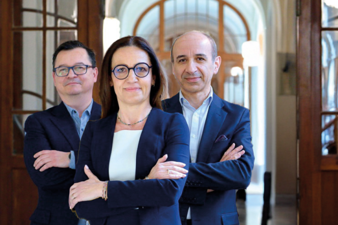 Trzy osoby stojące na tle korytarza Gmachu Głównego PG. Kobieta na pierwszym planie, za nią dwóch mężczyzn