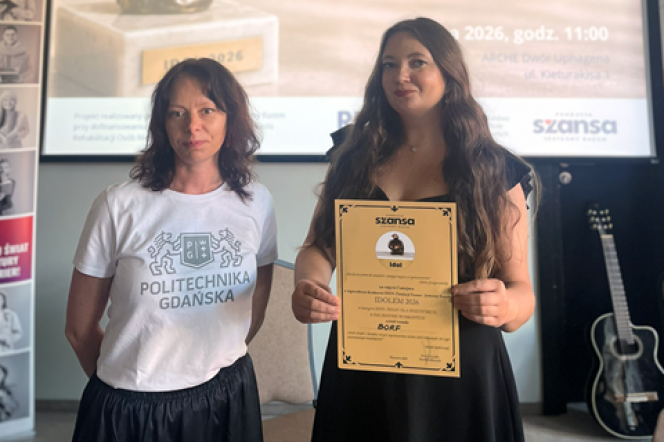 Dwie kobiety stoją na tle ekranu, jedna trzyma dyplom z napisem „Idolem 2026”, druga ma na sobie koszulkę z napisem „Politechnika Gdańska”.