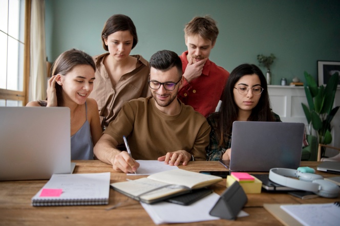 Kandydaci na studia siedzą przy biurku i pracują przy komputerach