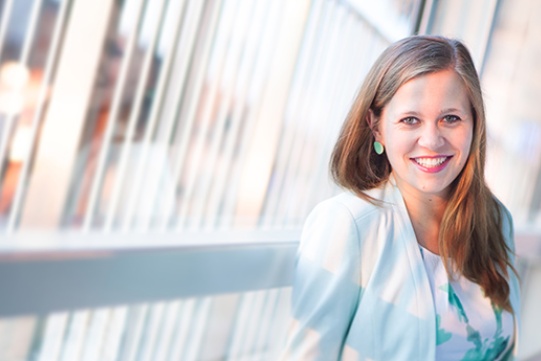 Na zdjęciu znajduje się dr inż. arch. Weronika Mazurkiewicz. Kobieta o ciemno blond długich włosach ubrana jest w białą marynarkę oraz biało zieloną bluzkę, pięknie się uśmiecha.