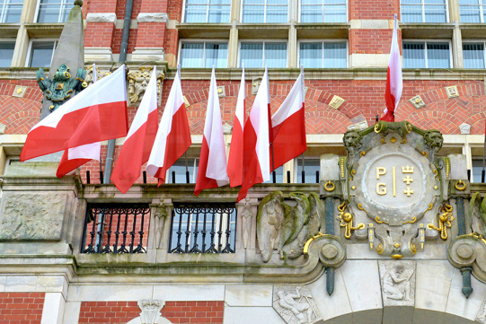 Na zdjęciu widoczny fragment Gmachu Głównego z kartuszem i biało-czerwonymi flagami nad wejściem głównym