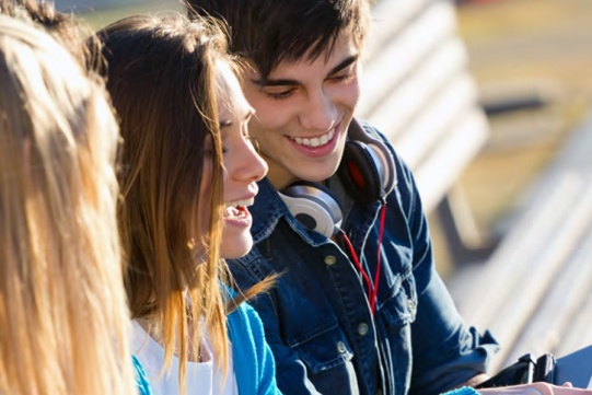 zdjęcie przedstawia dwoje młodych ludzi, widać uśmiechniętą twarz chłopaka i uśmiechniętą dziewczynę sfotografowanąz profilu