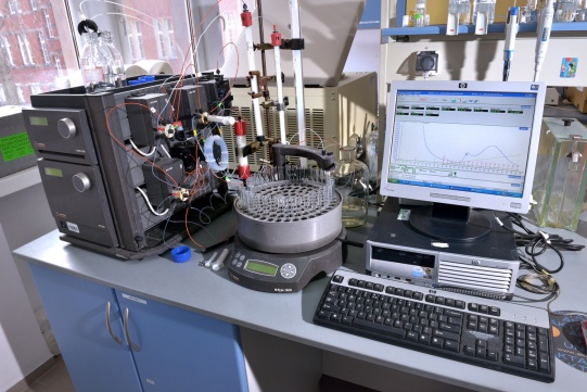 Zdjęcie przedstawia stanowiko pracy. Na zdjęciu widoczne jest biuro z komputerem, klawiatura i monitorem oraz aparatura z probówkami