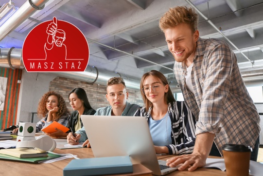 Na zdjęciu znajduje się grupa studentów ubrana w różne stroje. Siedząc przy stołach współpracują ze sobą.