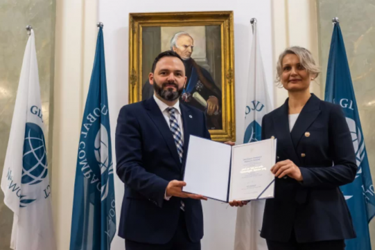 Dwie osoby trzymające dyplom nominacji do Rady stojące na tle obrazu 