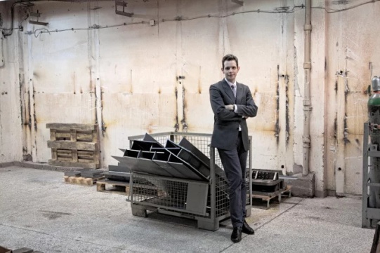 Na zdjęciu widoczny jest Krzysztof Wołoszyk ubrany w szary garnitur. Stoi w laboratorium.