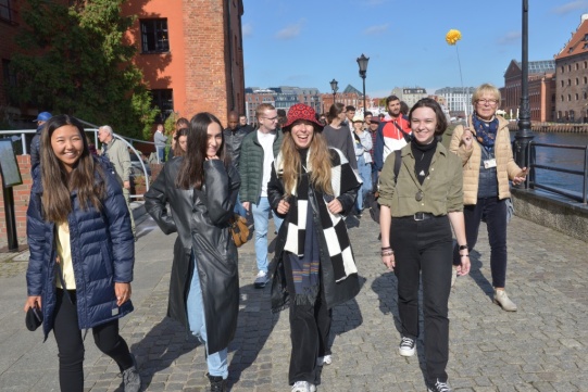 Grupa studentów spaceruje deptakiem wzdłuż rzeki.