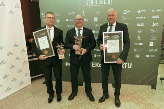 Trzech mężczyzn w garniturach trzyma statuetki i dyplomy.