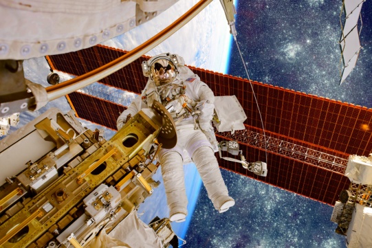 W przestrzeni kosmicznej osoba w skafandrze naprawia urządzenia.