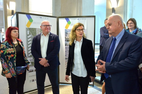 Na tle wystawy stoją elegancko ubrane osoby.