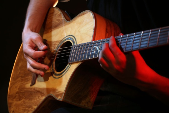 Gitara akustyczna trzymana przez dwie męskie ręce