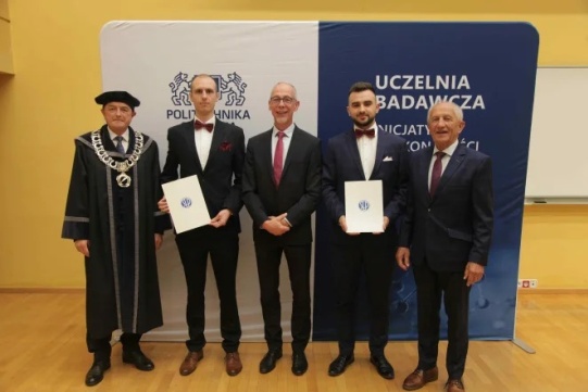 Na zdjęciu widoczna jest grupa mężczyzn, absolwentów oraz profesorów ubranych na galowo