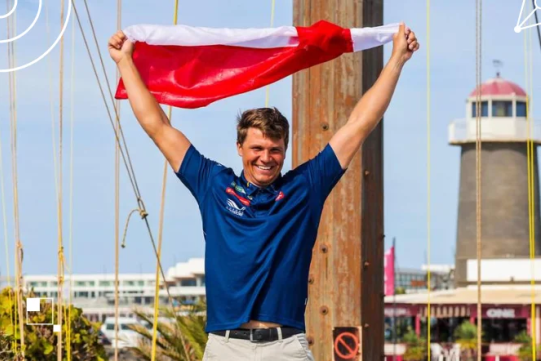 Na zdjęciu znajduje się mężczyzna w granatowej koszulce z czerwoną flagą