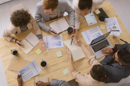 Ludzie siedzą w kółko przy laptopach.