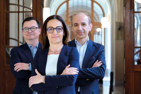 Trzy osoby stojące na tle korytarza Gmachu Głównego PG. Kobieta na pierwszym planie, za nią dwóch mężczyzn