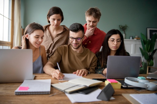 Kandydaci na studia siedzą przy biurku i pracują przy komputerach