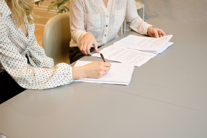 Na zdjęciu widać dwie kobiety w biurze podpisujące dokumenty. 